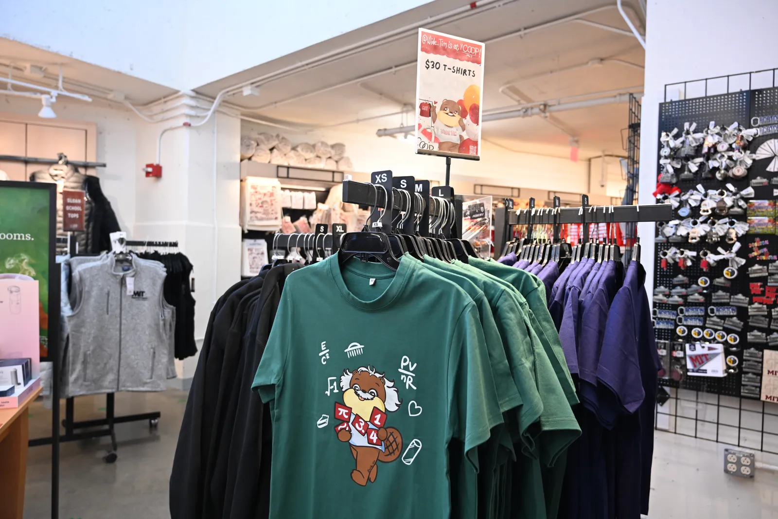 A rack of green Wide Tim t-shirts at the MIT COOP under a sign reading "@Wide_Tim is at the COOP!"